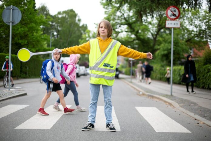 Skolepatrulje hjælper børn sikkert over vejen i morgentrafikken som led i kampagne om trafiksikkerhed.