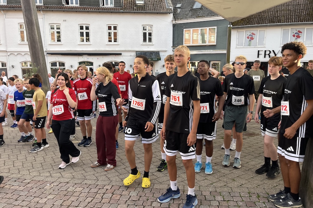 Løbere deltager i Hadsundløbet gennem byens gader med målområde på torvet og mange tilskuere i sensommervejr.