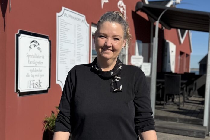 Charlotte Andersen står foran Havnens Fisk i Øster Hurup, hvor hun byder gæster velkommen til frisk fisk og hyggelig stemning ved havnen.